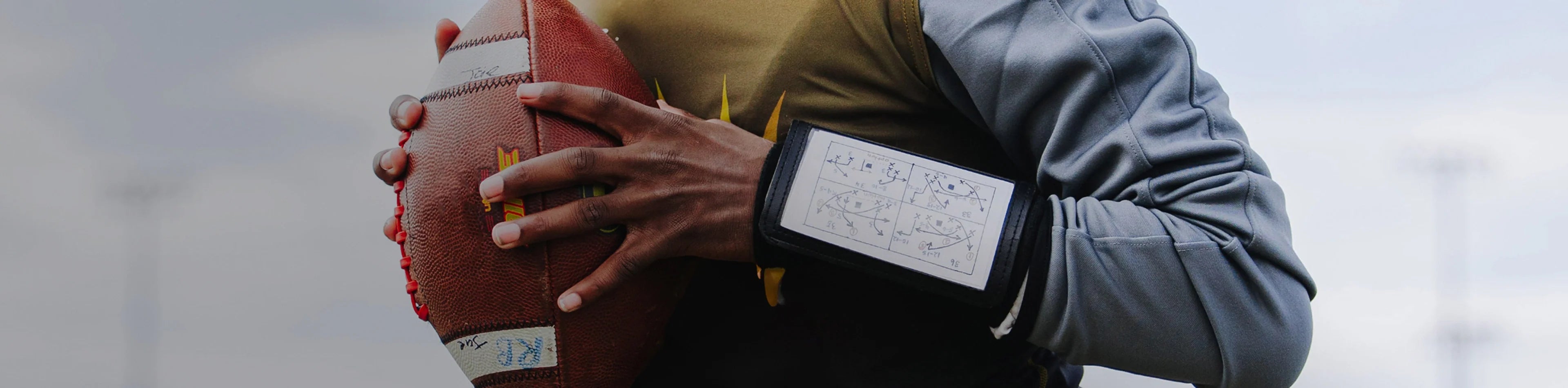 Header image for the 'Football Accessories' Collection by Cutters Sports. A player grips a football while wearing a wrist coach playbook sleeve, highlighting essential gear for on-field performance.