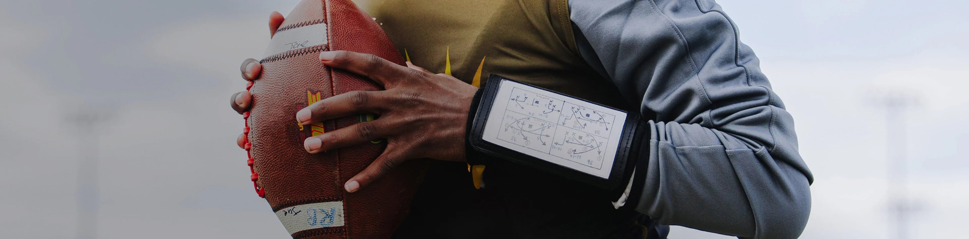Header image for the 'Football Accessories' Collection by Cutters Sports. A player grips a football while wearing a wrist coach playbook sleeve, highlighting essential gear for on-field performance.