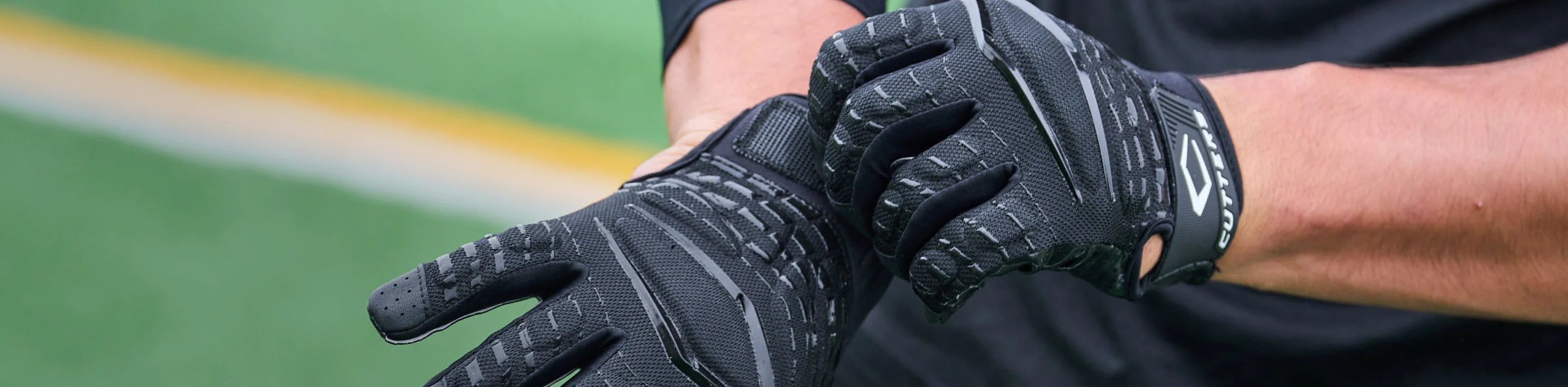 Header image for the 'Outlet' Collection by Cutters Sports. A close-up of a player tightening black Cutters football gloves on a turf field, highlighting discounted performance gear.