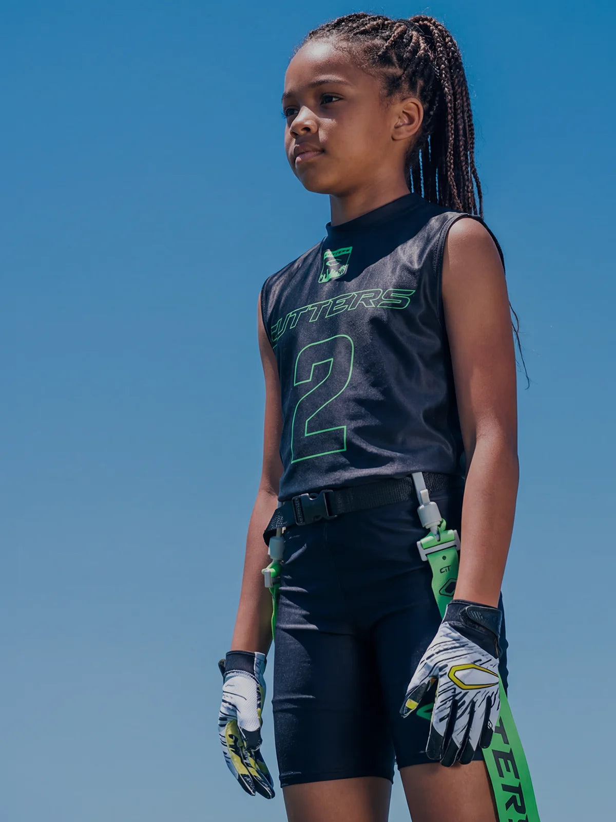 Two youth athletes wearing sports uniforms with football gloves and a clear blue sky background
