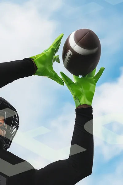 Person wearing green gloves catching a football against a blue sky.