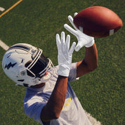 Football receiver reaching overhead to catch a pass wearing white Cutters Rev Pro 7.0 Solid receiver gloves on a turf field