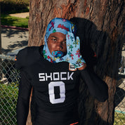 Football player leaning against a tree wearing Blue Divine Drip Game Day Pro receiver gloves, with a matching Divine Drip skull wrap and mouthguard
