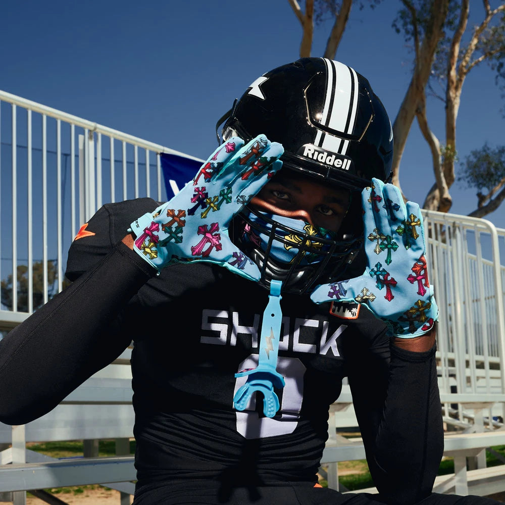 Person wearing a black football helmet and gloves with colorful designs, standing outdoors.