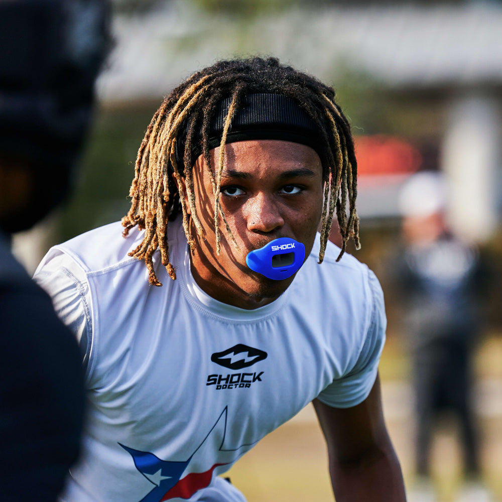 Football player in white uniform wearing a royal blue Shock Doctor Max AirFlow Lip Guard during game action.