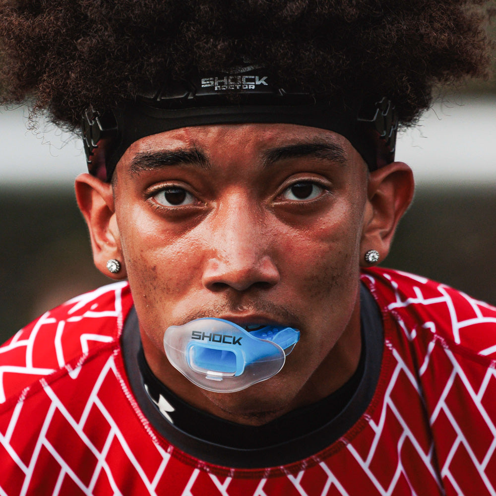 Football player in red patterned uniform wearing a translucent blue Shock Doctor Max AirFlow Lip Guard during game play.