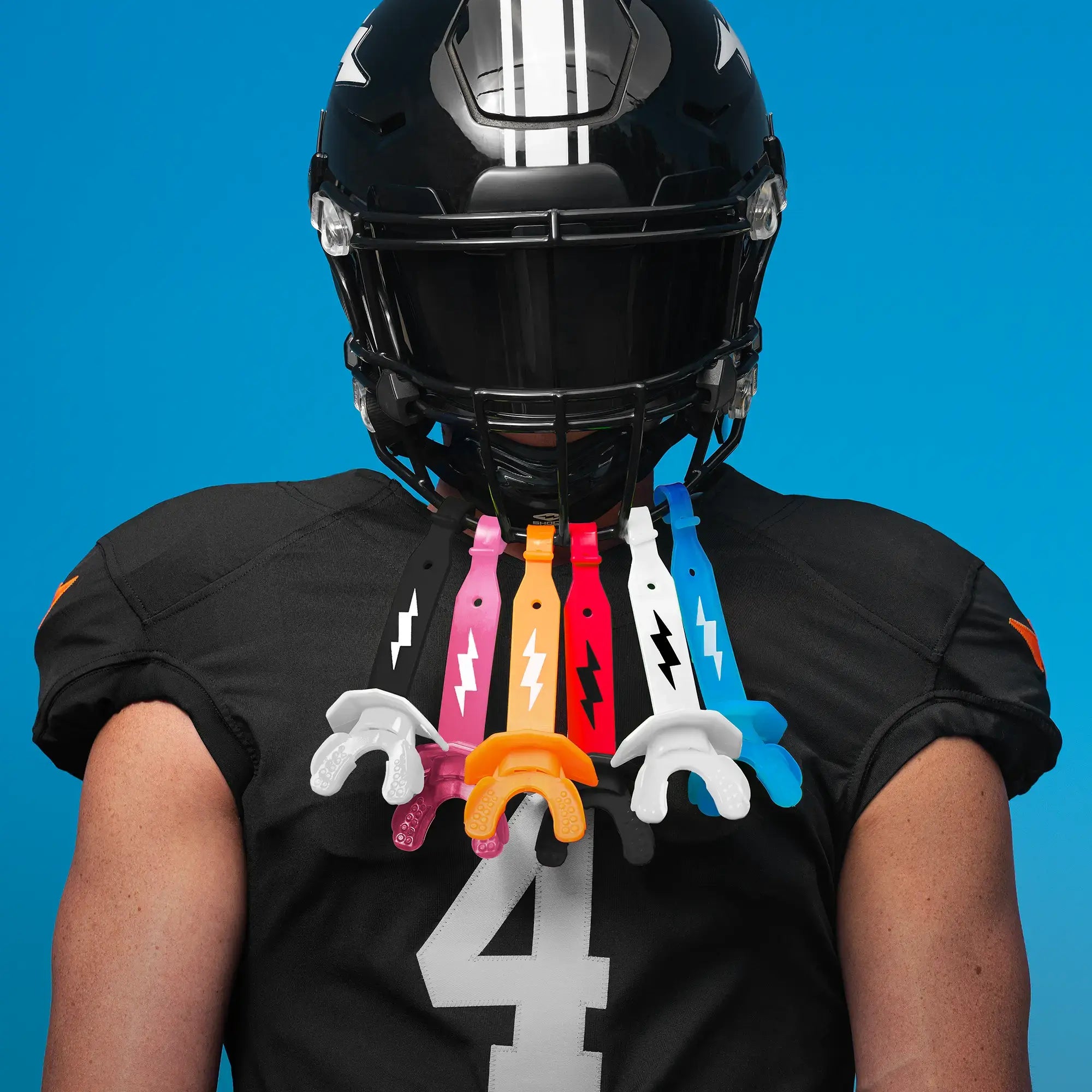 Person wearing a black football helmet and jersey with colorful mouthguards on a blue background