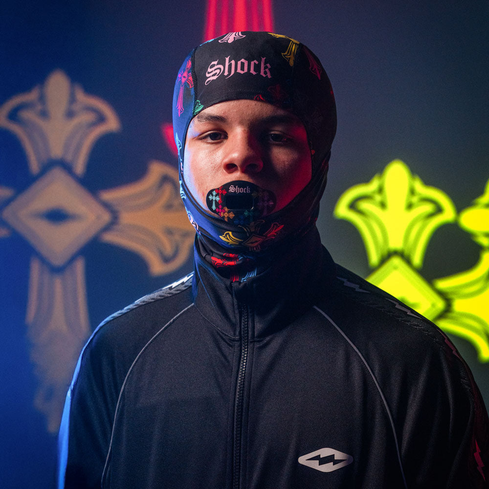 Person wearing a colorful sheisty ski mask and black jacket with a logo, standing against a dark background with neon designs.